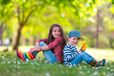 Happy kids boy and girl in rain rubber boots playing outside in the green park with blooming field of daisy flowersの写真素材
