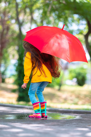 Happy beautiful girl with umbrella and color rubber boots jump on a rainy puddleの写真素材