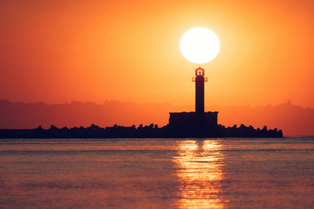 Seascape of sunrise over sea lighthouse and coastal beach shore, Varna, Bulgariaの写真素材