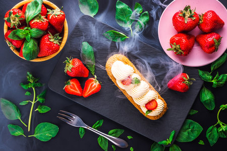 French eclair grazed with chocolate and fruity strawberry cream or sweet Italian profiteroles and fresh juicy strawberries, food on black backgroundの写真素材