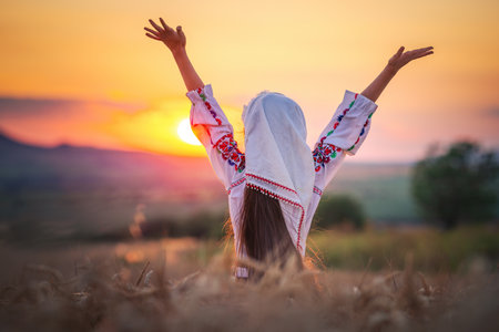 Farmer woman bulgarian little girl in ethnic folklore costume hold golden wheat straws and sickle in harvest field, harvesting and agriculture in Bulgariaの写真素材