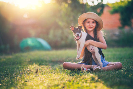 Happy girl playing with cute playful puppy little dog outdoor on a sunny day in a parkの写真素材
