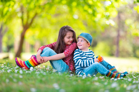 Happy kids boy and girl in rain rubber boots playing outside in the green park with blooming field of daisy flowersの写真素材