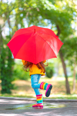 Happy beautiful girl with umbrella and color rubber boots jump on a rainy puddleの写真素材