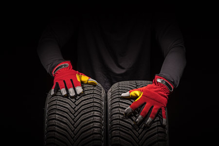 Car tire service and hands of mechanic holding new tyre on black background with copy space for textの写真素材