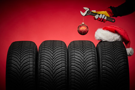 Winter car tires service and hands of mechanic, wrench screwdriver, christmas ball happy new year red backgroundの写真素材