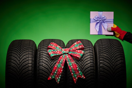 Car tires, new tyres, winter wheels, hand of man with present box with bow isolated on green background with bow ribbon present.の写真素材