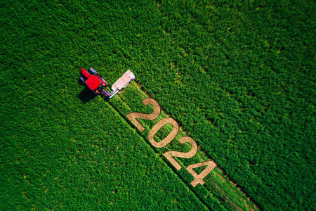2024 Happy Ney Year concept and red tractor mowing green field.の写真素材