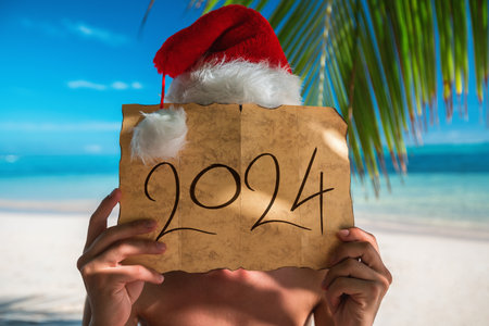 2024 Happy New Year fom summer destination. Tourist man with Santa Claus hat relaxing on tropical island beach Punta Cana, Dominican Republicの写真素材
