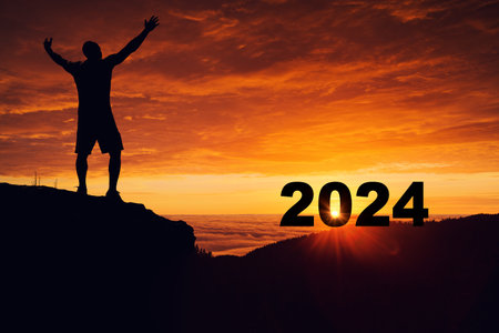 Man silhouette on the mountain top watching the sunrise horizon celebrating new year 2024.の写真素材