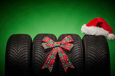 Car tires, new tyres, winter wheels isolated on green background with bow ribbon present and Santa claus hat.の写真素材