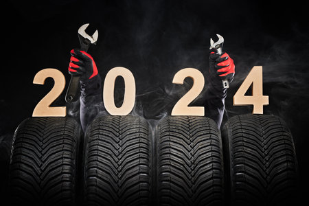 Car tires, winter wheels, new tyres in fog and hands of mechanic with wrench instruments, happy new year 2024 black background .の写真素材
