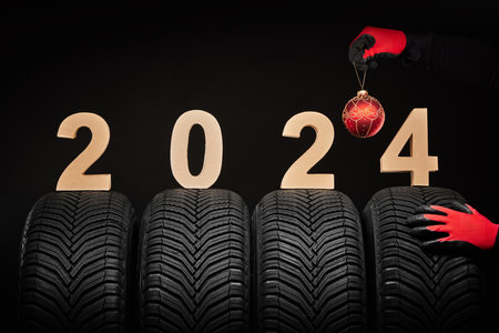 2024 happy new year, winter care tires and hands of a man with christmas tree ball on black backgroundの写真素材
