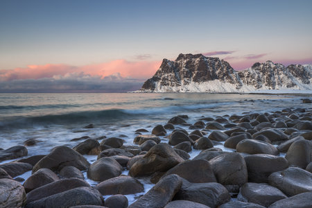 Seascape of rocky beach coast and mountain peaks with snow, scenic winter sunset over the seaの写真素材