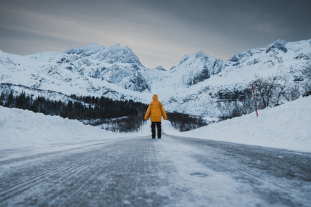 Scenic Winter Arctic Landscape with car trails in frozen Road Leading to Snowy Mountain Peaks and person on the path to the climb. Lofoten, Norwayの写真素材