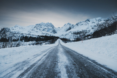 Scenic Winter  Landscape with car trails in frozen Road Leading to Snow Capped Mountain Peaks. Lofoten, Norwayの写真素材