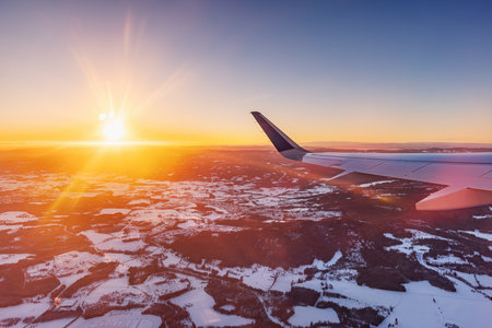 Airplane flying low over snowy mountains and preparing for landing to the airport, view from plane window of wing turbine and skylineの写真素材