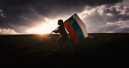 Woman in ethnic folklore costume waving Bulgarian flag on a sunset green field celebrating independence and liberationの写真素材
