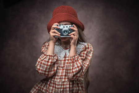 Retro portrait of caucasian girl dressed in vintage dress and hat with old retro camera against a brown leather backgroundの写真素材
