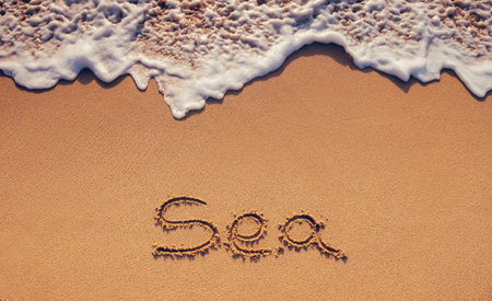Sea handwritten text on the beach sand of tropical island coast and ocean wave as nature backgroundの写真素材