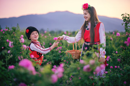 Bulgarian rose valley near Kazanlak, Bulgaria and girl and boy sibling in ethnic folklore clothes...