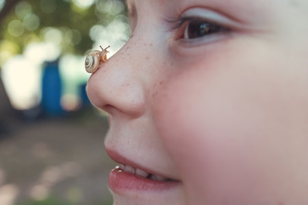 Child Smiling with a Snail on Their Nose in a Bright Gardenの写真素材
