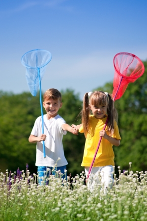 Happy boy and little girl with butterfly nets walking on a meadow in a sunny dayの写真素材