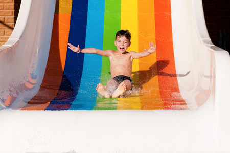 Boy has into pool after going down water slide during summerの写真素材