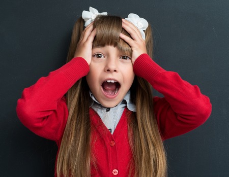 Portrait of shocked little girl at the black chalkboard in classroom.の写真素材