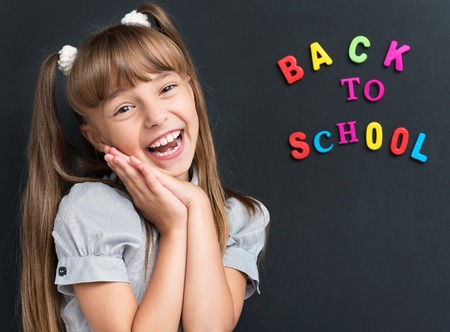 Photo of adorable young cheering girl looking at camera at the black chalkboard in classroom.