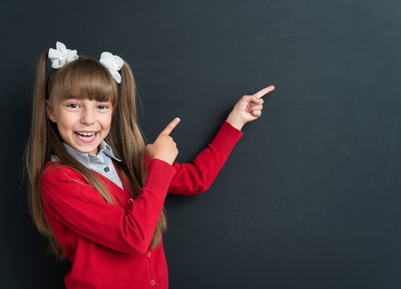 Little excited girl pointing at something at the black chalkboard in classroom.の写真素材