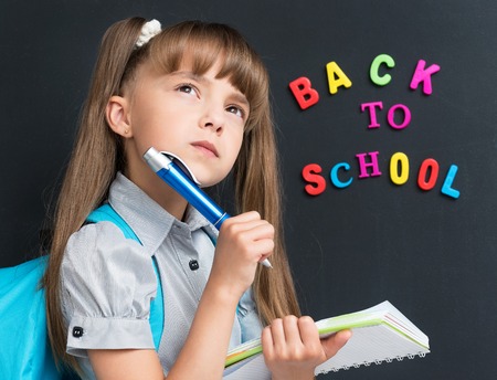 Little schoolgirl thoughtful about something at the black chalkboard in classroom