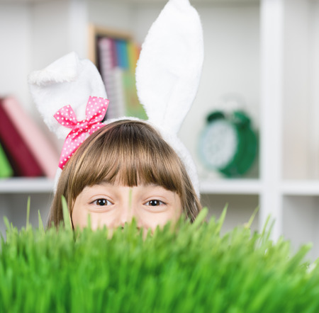 Beautiful little girl dressed in Easter bunny ears peeking from behind the green grass