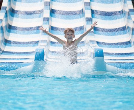 Boy has into pool after going down water slide during summerの写真素材