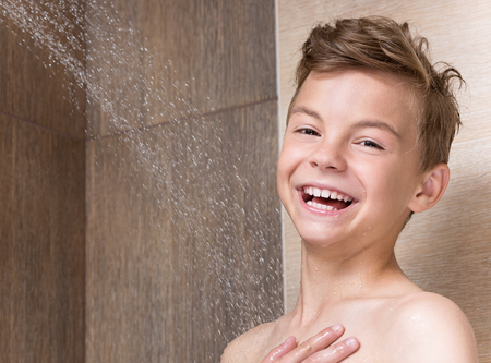 Cheerful boy washing face and body in shower in the bathroomの写真素材