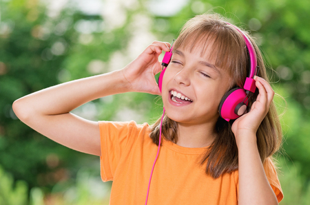Little girl with headphones listening to music in summer parkの写真素材