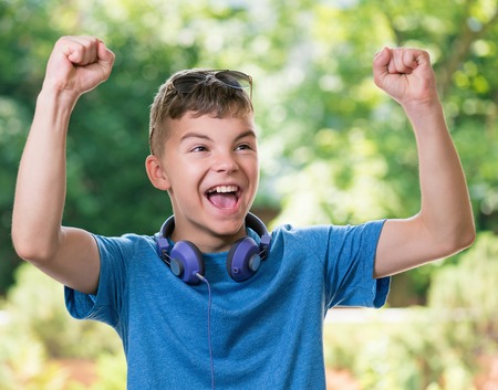 Victory screaming teen boy 12-14 year old. Winner boy with headphones and sunglasses posing outdoors.の写真素材