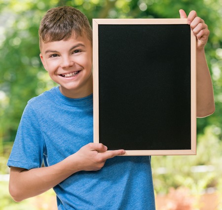 Outdoor portrait of happy teen boy 12-14 year old with small blackboard. Back to school concept.の写真素材