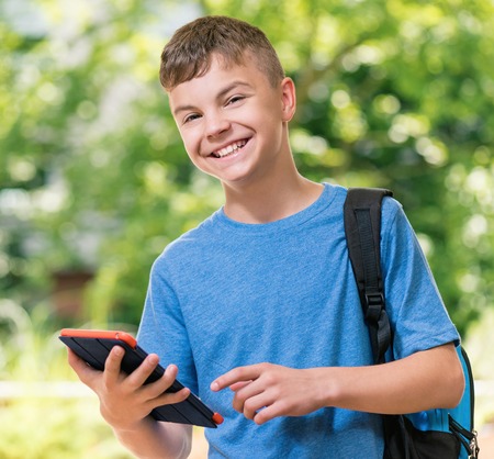 Outdoor portrait of happy teen boy 12-14 year old with tablet. Schoolboy watching media content in a tablet at park.の写真素材