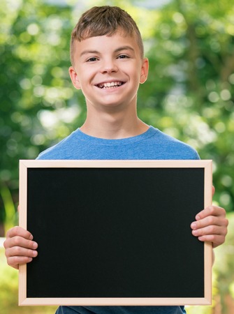 Outdoor portrait of happy teen boy 12-14 year old with small blackboard. Back to school concept.の写真素材