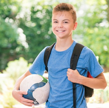 Outdoor portrait of happy teen boy 12-14 year old with soccer ball and backpack. Back to school concept.の写真素材