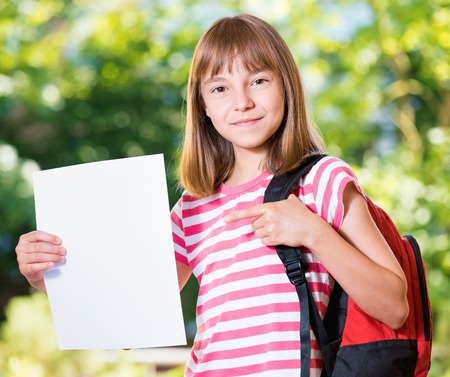 Outdoor portrait of happy girl 10-11 year old with white blank and backpack. Back to school concept.の写真素材