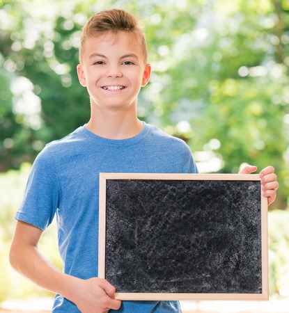 Outdoor portrait of happy teen boy 12-14 year old with small blackboard. Back to school concept.