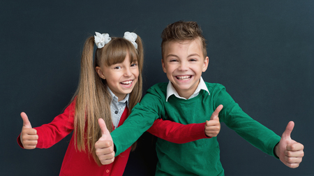 Happy pupils - boy and girl, showing thumbs up gesture in front of a big chalkboard. Back to school concept.の写真素材
