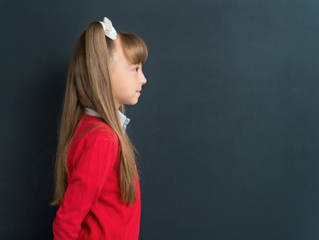 Side view photo of happy girl 10-11 year in front of a big chalkboard. Back to school concept.の写真素材