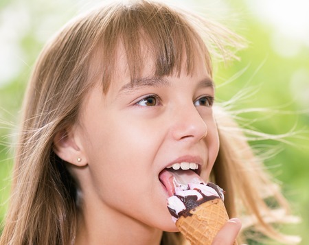 Happy girl 10-11 year old eating ice cream cone. Outdoor portrait.の写真素材