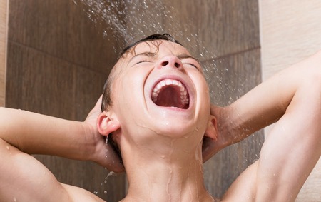 Happy teen boy bathing under a shower - washing head, in the bathroom at homeの写真素材