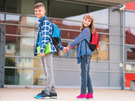 Happy children - boy and girl with books and backpacks on the first school day. Young students beginning of class after vacation. Full length outdoor portrait in yard.の写真素材