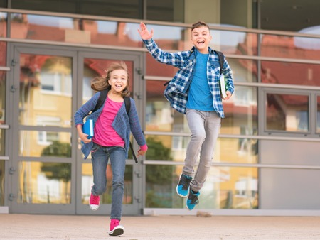 Happy children - boy and girl with books and backpacks on the first school day. Excited to be back to school after vacation. Full length outdoor portrait.の写真素材