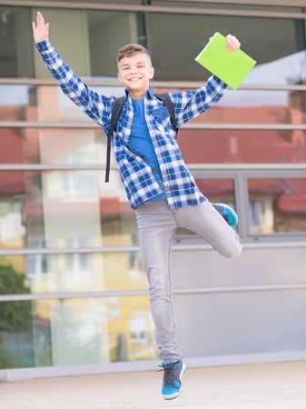 Happy teen boy with book and backpack on the first school day. Excited to be back to school after vacation. Full length outdoor portrait.の写真素材
